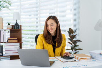 Smiling Businesswoman Working: A young, smiling businesswoman works diligently at her desk, using a...