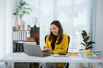 Focused Female in Office: A dynamic businesswoman, radiating confidence in a yellow blazer, engages with her laptop and notes. A scene of organized productivity in a modern office setting. 
