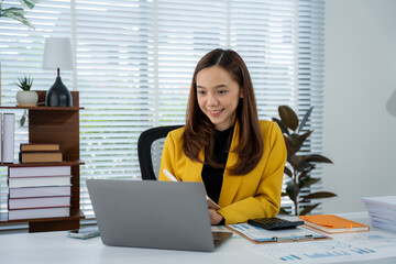 Working Woman at Desk: A woman, elegantly dressed in a yellow blazer, works diligently at her desk,...