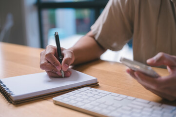 Close-up of Man Writing in a Notebook at a Desk, A person writes in a notebook with a pen while...