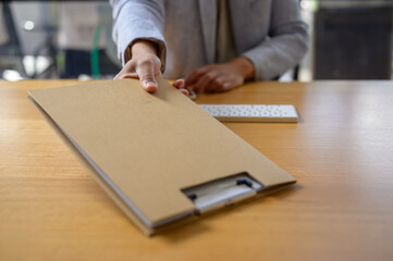 Close-up of a businessperson's hand reaching for a confidential folder on an office desk,...