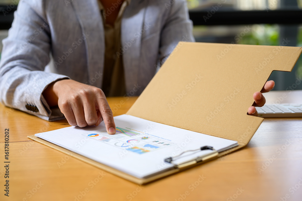 Poster close-up of a businessperson pointing at financial data and colorful graphs in a report folder. conc
