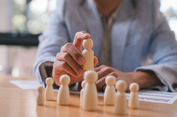 Close-up of a businessman selecting a wooden human figure from a group, symbolizing recruitment,...