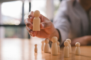 Close-up of a businessman selecting a wooden human figure from a group, symbolizing recruitment,...