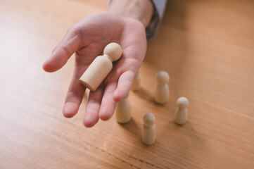 Close-up of a businessman selecting a wooden human figure from a group, symbolizing recruitment,...