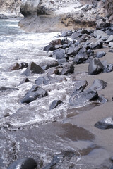 Rocky shoreline with smooth wet sand, waves with foam gently lapping against grey stones, creating a serene coastal atmosphere, showcasing natural colors in a tranquil environment. Vertical background