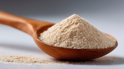 A wooden spoon filled with a beige powdery substance some of which has spilled onto the white surface below