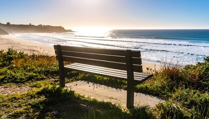 Serene coastal view; empty bench overlooks sandy beach and ocean waves at sunset