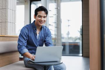 Fototapeta premium Asian freelancer working remotely on laptop in coworking space