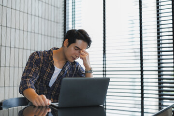 Stressed asian freelancer suffering headache working from home office