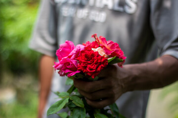 A man holds a bunch of flowers, and the background is blurred