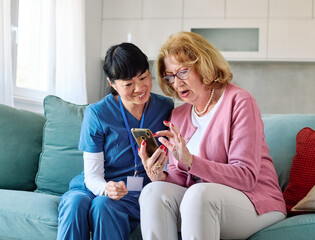 Doctor or nurse caregiver helping senior woman with a mobile phone at home or nursing home