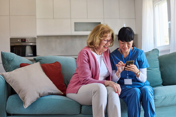 Doctor or nurse caregiver helping senior woman with a mobile phone at home or nursing home