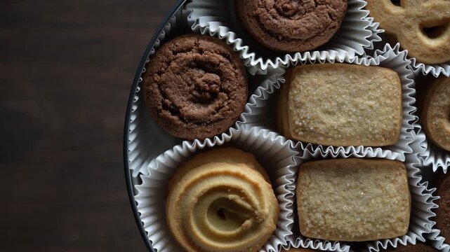 Crispy crumbly shortbread cookies in a round metal box on wooden table, top view, close up, rotates