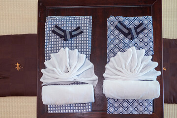 Japanese ryokan style yukata robes neatly folded on wooden table with white towels arranged to rest...