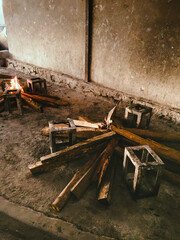 A low-angle shot depicts firewood and small concrete stools arranged near a burning fire in a...