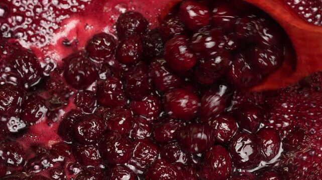 Preparing freshly picked red cherries with sugar to make cherry jam in a saucepan with a wooden spoon, close up. Cooking berries marmalade, home cooking