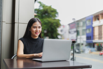 Asian freelancer working remotely on laptop in outdoor cafe