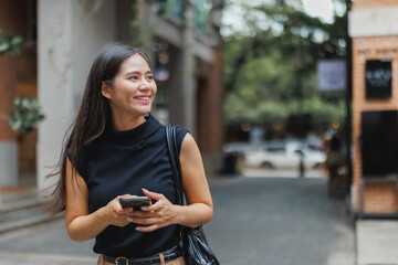 Smiling businesswoman walking down the street holding smartphone
