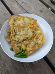 A plate of traditional Indonesian corn fritters, known as corn fritters, served with fresh green chili peppers. This savory snack features sweet corn kernels in a crispy, golden-brown batter.