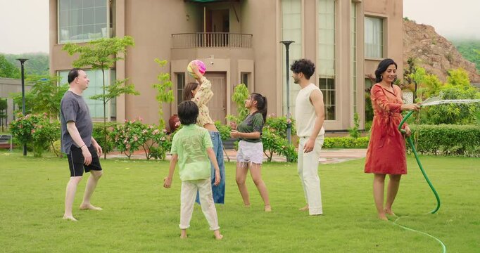 Indian happy mom man hold hose pipe spray water on house lawn park tree young adult family teen girl dad cute son kid boy child male female group play ball game have fun joy spend time enjoy trip day - Powered by Adobe