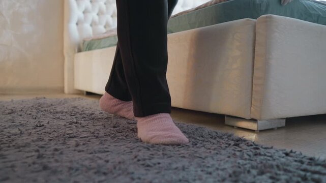 Close-up of elderly woman s feet in pink socks walking on soft shaggy rug next to bed in peaceful bedroom, soft lighting, calm atmosphere, minimalistic room design, cozy and relaxed home setting