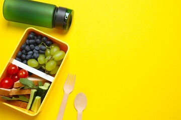 Top view photo of lunch box with healthy snacks, fruits and  bottle of water on a yellow background