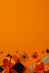 Halloween seasonal composition with gift boxes, pumpkins and decorations on bright orange...