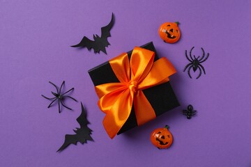 Flat lay on purple background with gift, pumpkins, bats and spiders. Halloween concept
