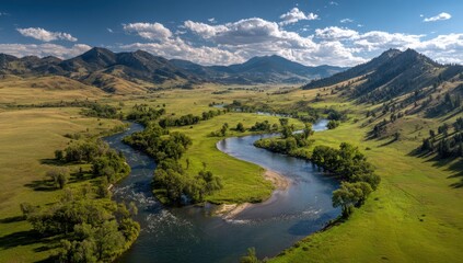 Fototapeta premium Panoramic vista of a winding river through a valley, surrounded by rolling hills and grasslands under a partly cloudy sky