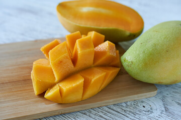 Mango slices on a cutting board on a white wooden table.