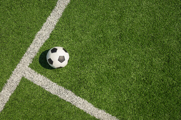 Soccer ball on green grass field with white line corner. Football stadium background. View from...