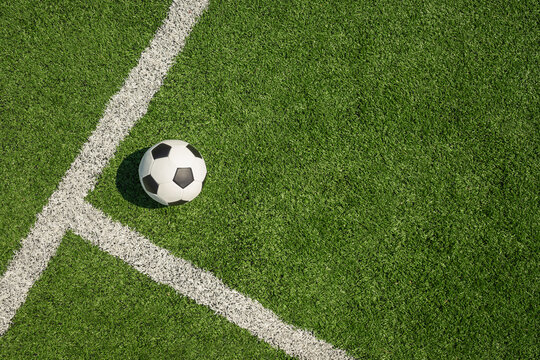Soccer ball on green grass field with white line corner. Football stadium background. View from above.