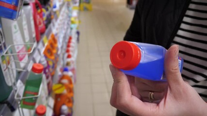 Close-up of white young woman's hands holding a jar of blue liquid for cleaning a washing machine, dishwasher or other household appliances, reading the description before buying and choosing in a - Powered by Adobe