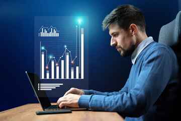 Professional man analyzes data on laptop in modern workspace with digital graphs during evening