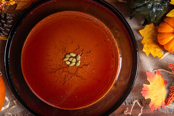 A glistening pumpkin flan, adorned with pumpkin seeds, sits on a dark plate.