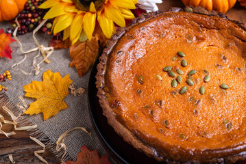 Pumpkin pie topped with pumpkin seeds, on a wooden table, surrounded by autumn leaves and sunflowers