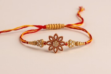 A close up view of a rakhi with a flower design on a white background with red and yellow thread