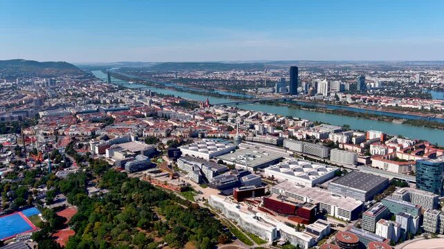 Dynamic aerial pan reveals Vienna&rsquo;s Messe Wien expo halls, DC Tower, Reichsbr&uuml;cke and the shimmering Danube slicing past Donauinsel, with St Francis Church framed by a crystal‑clear summer sky.