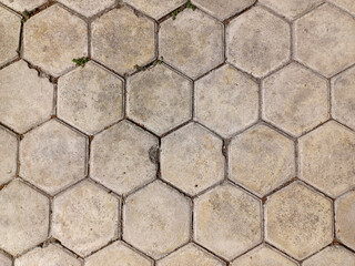 Textured surface made of hexagonal concrete pavers. The pavers are light grey, showing signs of...
