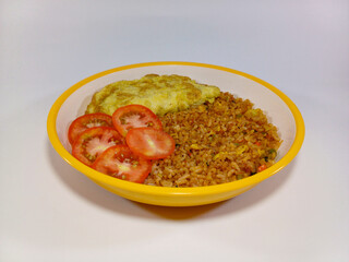 A vibrant plate of Indonesian fried rice, or Nasi Goreng, mixed with fresh red tomatoes, and omelet. Presented on a white background, relating to Indonesian cuisine, Asian food, comfort meal
