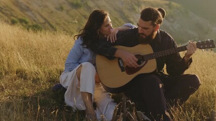 A couple enjoys a serene moment playing guitar in a picturesque, grassy landscape filled with natures charm - Powered by Adobe