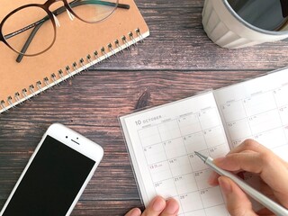 10月のスケジュール帳に記入する女性の手と机上のスマホ