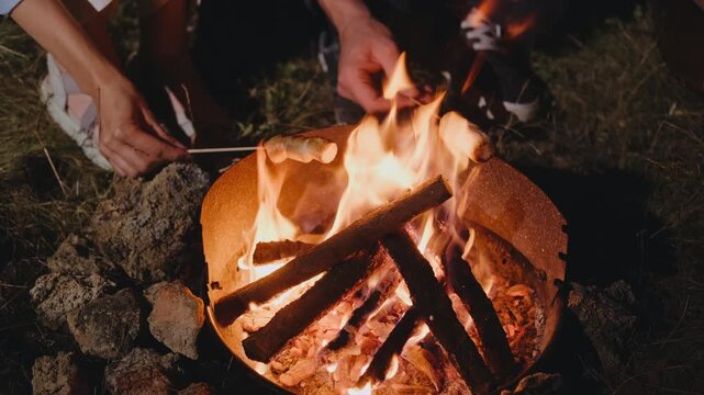 Delight in the comforting warmth of a glowing campfire while happily roasting marshmallows with friends at night