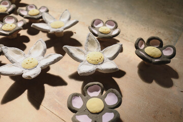 Clay flowers in pastels cast artistic shadows on wood under warm sunlight
