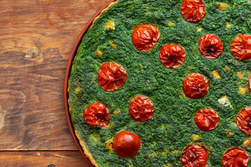 Freshly baked spinach and tomato pie on a wooden table, perfect for a healthy meal or snack in a...
