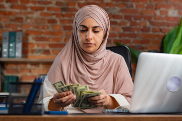 Woman in Hijab Counting Money at Her Office Desk
