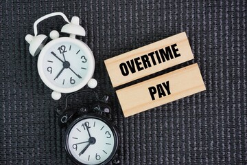 Two clock bells and a stick with the words Overtime pay. the concept of overtime or payment by time