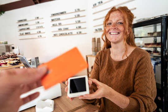 Cafe owner processing credit card payment for customer at counter