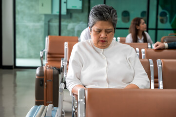 Senior female traveler sitting in airport hall waiting onboard 